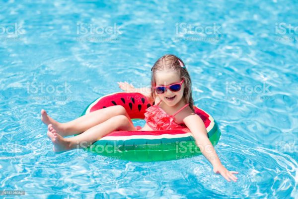 Child with watermelon inflatable ring in swimming pool. Little girl learning to swim in outdoor pool of tropical resort. Kid eye wear. Water toys and floats for kids. Healthy sport for children.